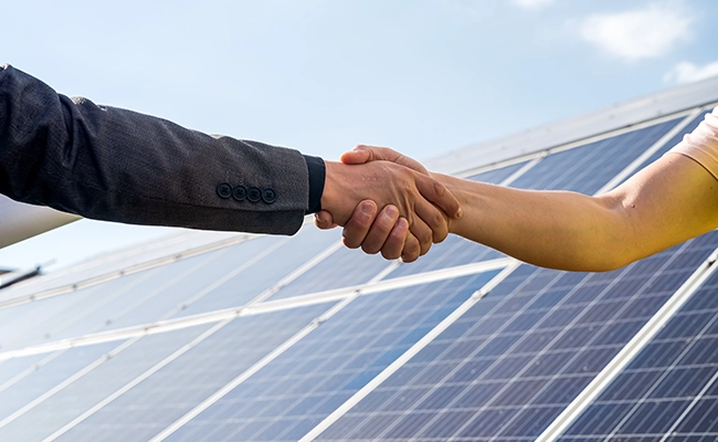 apertando as mãos com placas de energia solar ao fundo